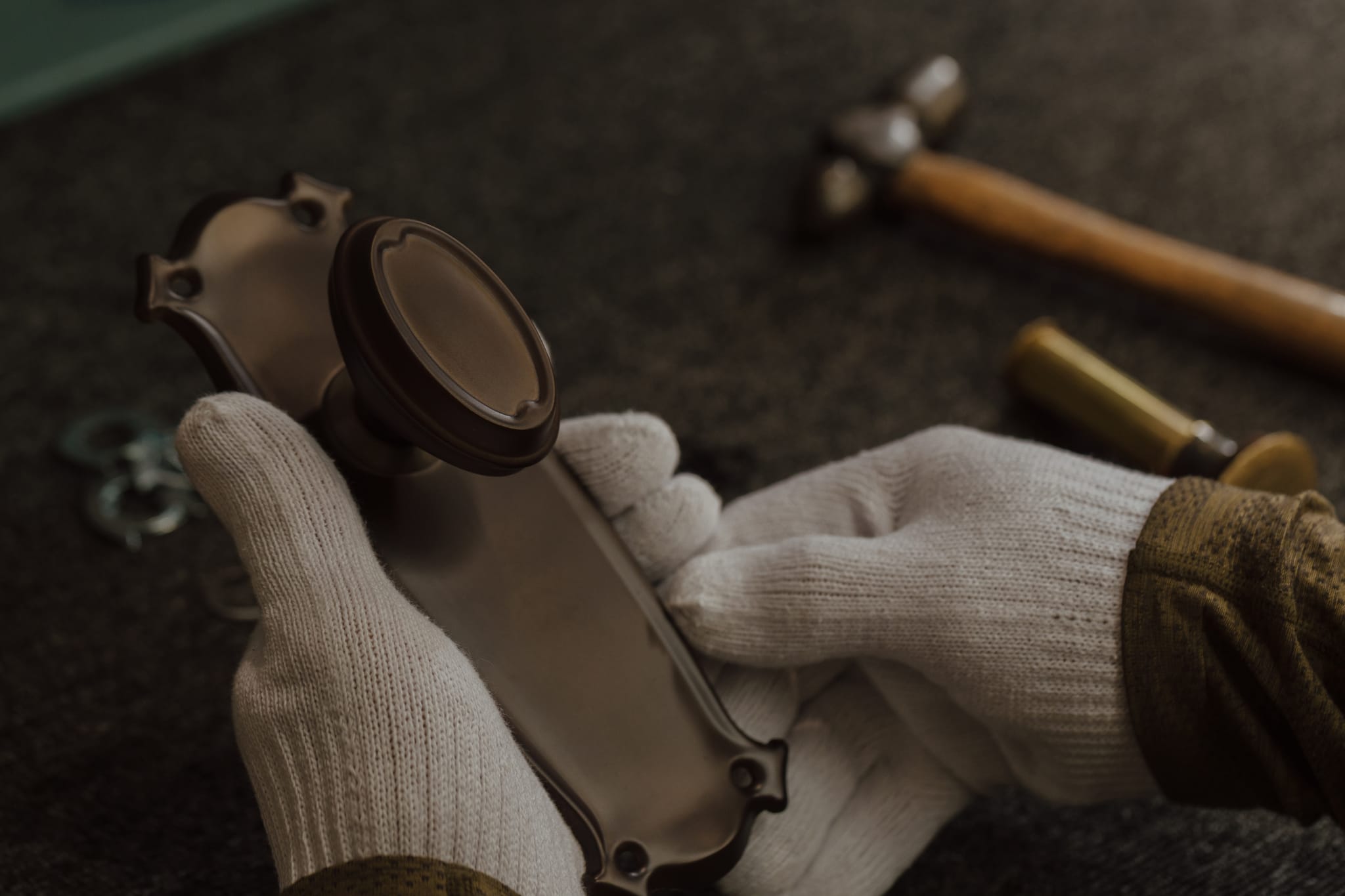 Gloved hands inspecting a cast brass backplate and knob at the bench