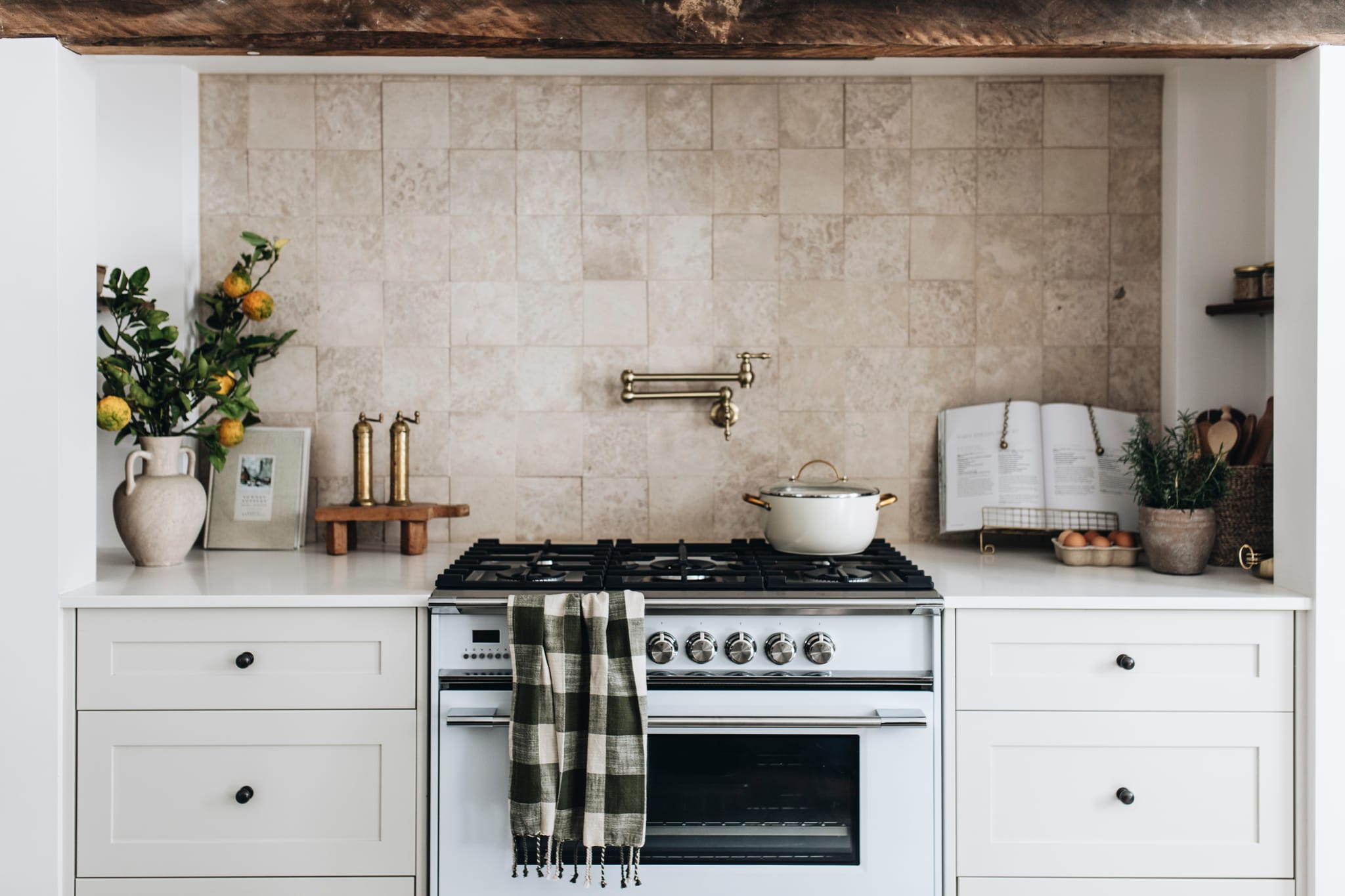 Limestone splashback kitchen with an aged brass pot filler and black cabinet knobs