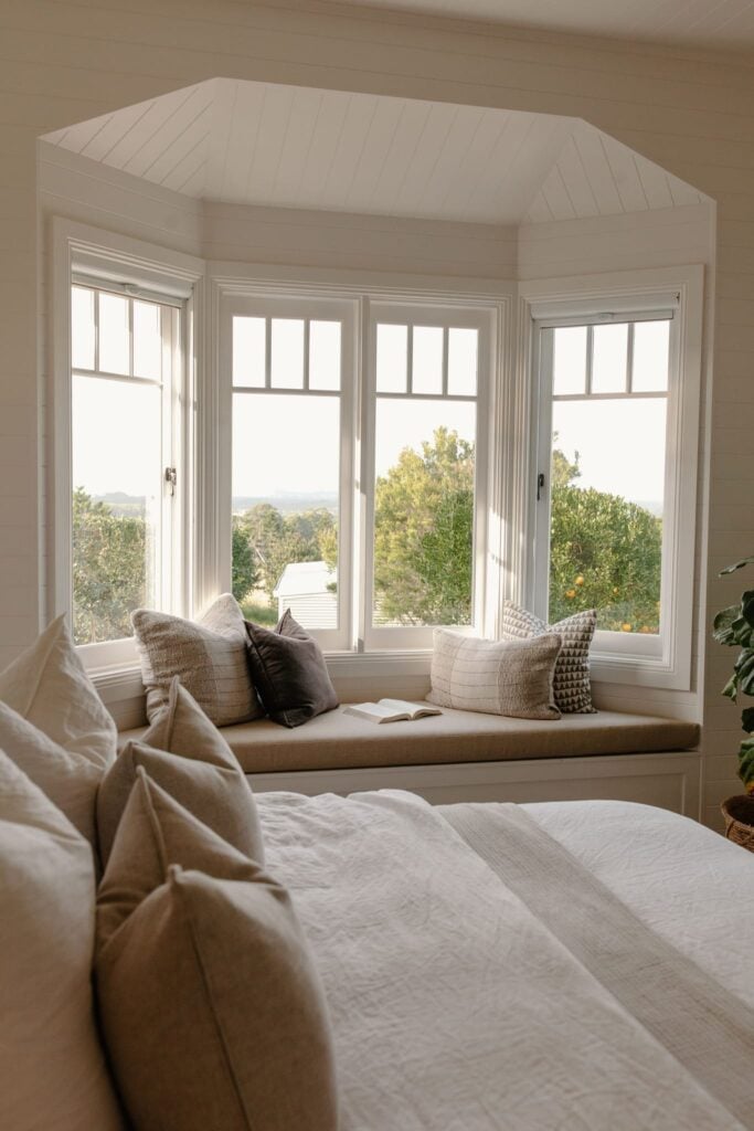 Bay of white timber casement windows above a window seat in a bedroom