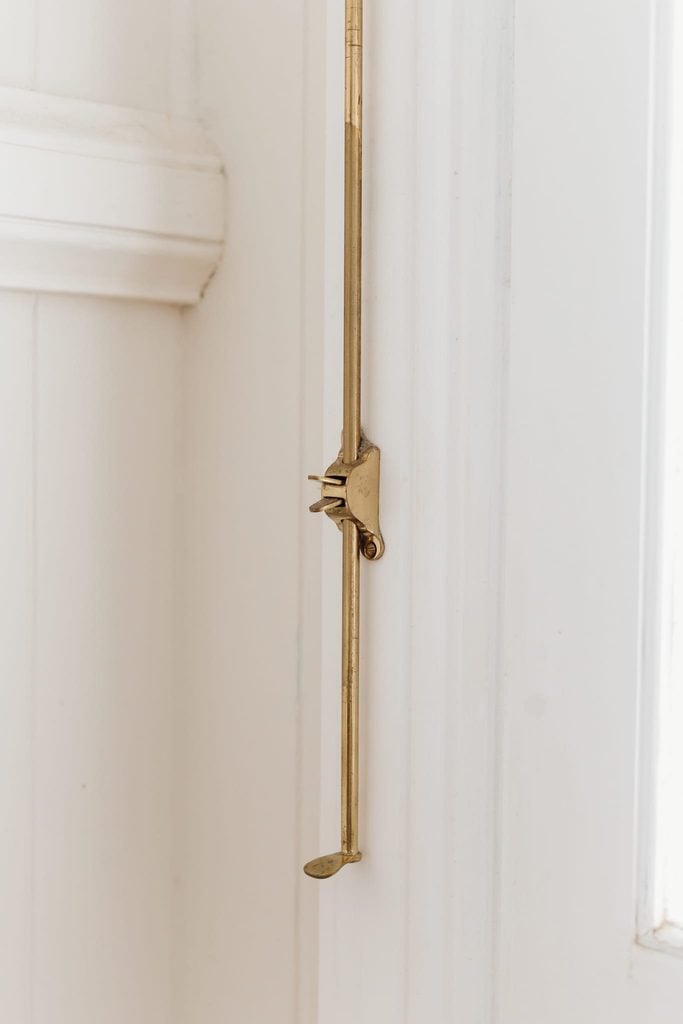 Brass fanlight window operator running down a white panelled wall