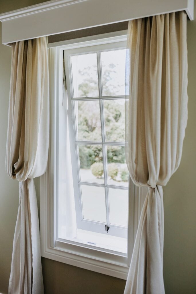 White timber awning window framed by linen curtains