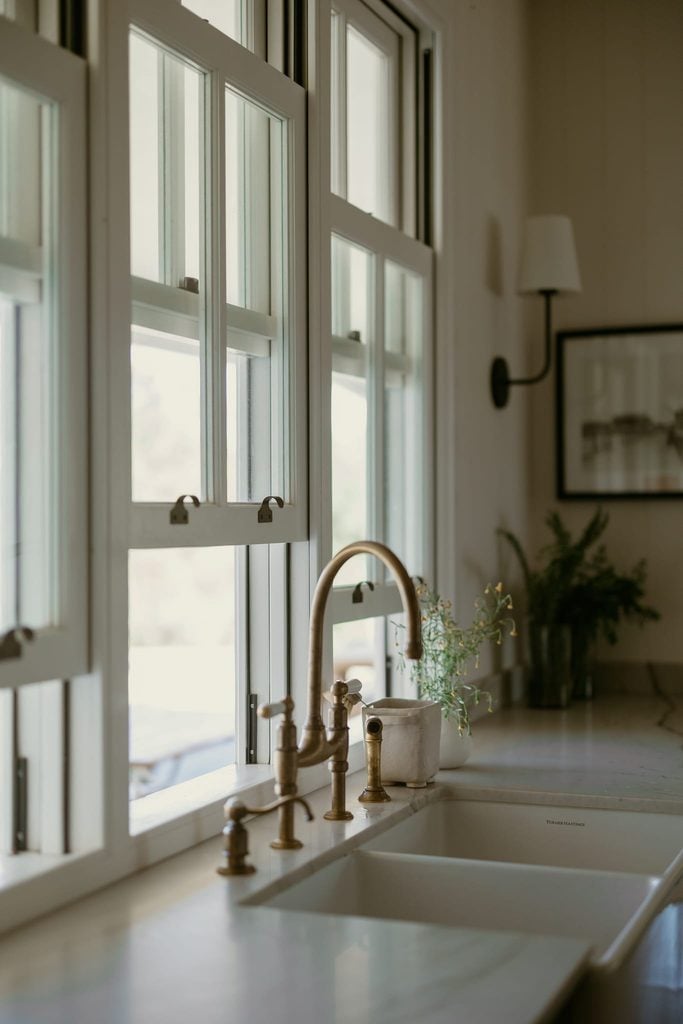 White timber sash windows above a farmhouse sink with brass tapware
